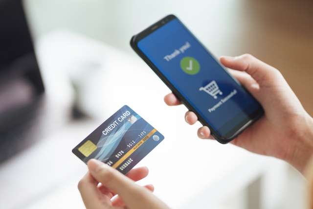 Young woman holding credit card and using smart phone for online